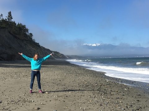 Person stands on rocky beach with arms extended high