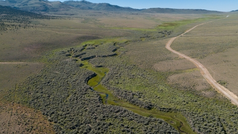 Aerial image of a water system flowing through the bottom of a dry valley. A dirt road follows the water across the valley.
