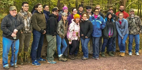 A group of about 20 dressed in warm clothes pose together in a forest