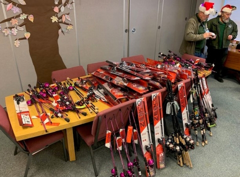 Service partners from Rods and Reels in Need and Washington Department of Fish & Wildlife standing behind more than 100 fishing rods donated for holiday charity gifts.