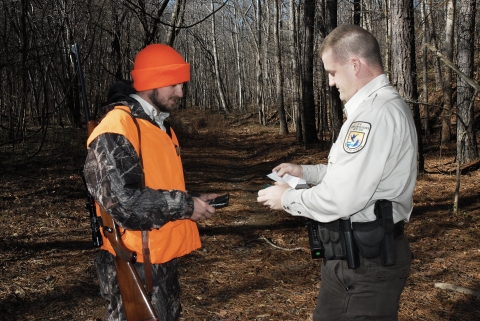 Law enforcement officer, in the woods, checking deer hunter's license and permit