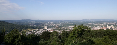 A landscape photo taken from a hilltop overlooks the town of Reading, Pennsylvania, below, with hills in the distance.
