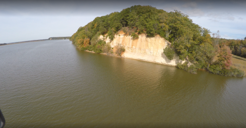 White cliffs capped with bright green trees. The cliffs are adjacent to a wide river. 