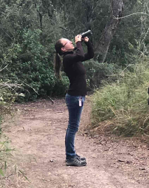 a woman uses binoculars on a wooded trail