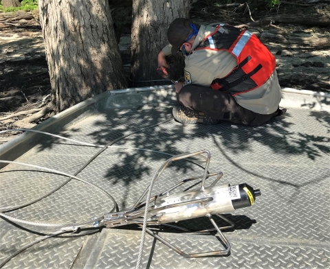 Biologist sits on boat to install telemertry receiver to tree