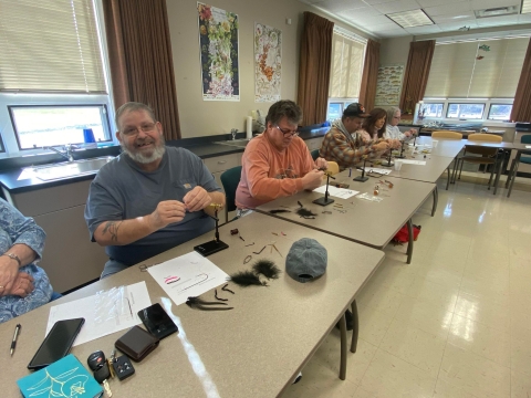People sitting at tables in a classroom tying flies