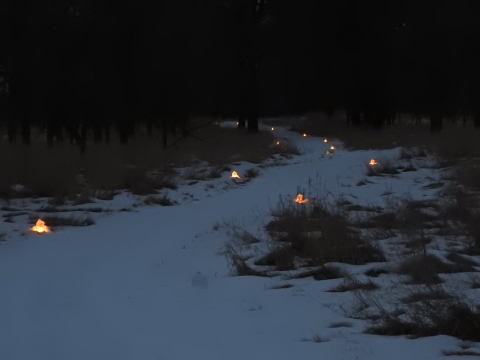 Snow covered trail with candles spaced out on the sides providing light