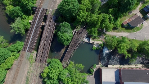 An aerial view of a river with a dam and three railroad bridges spanning it.