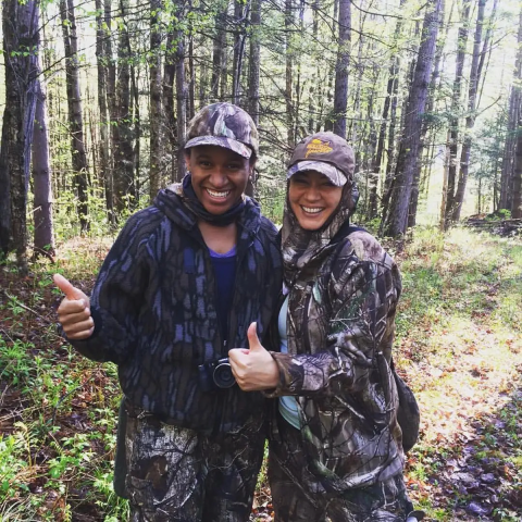 two people wearing camouflage in the woods give a thumbs up