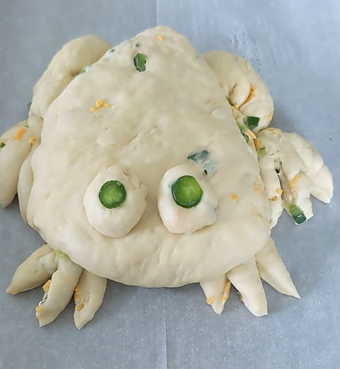 a ball of dough shaped into the body, hind legs, hind toes, front toes, and eyes of a frog. Two slices of jalapeno are used as irises for the eyes.