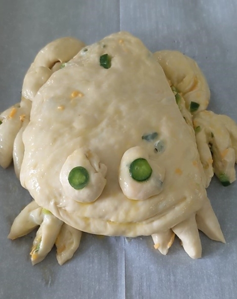 Dough shaped into a frog. It is brushed with eggwash.