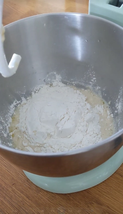 Flour being poured on top of a yeast mixture in a stand mixer