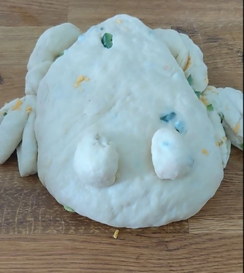 a ball of dough shaped into the body, hind legs, hind toes, and eyes of a frog