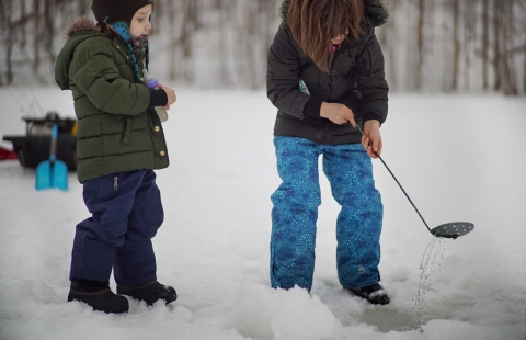 a girl and boy on the ice scooping out a hole