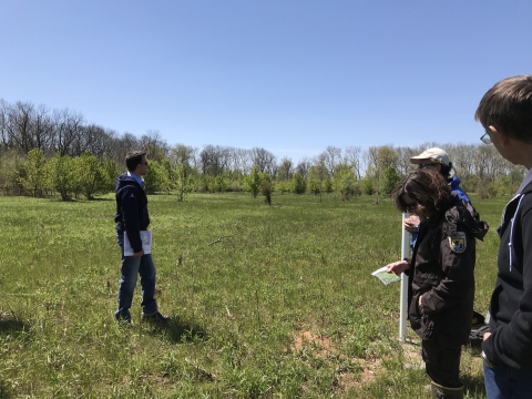 People standing in a grassy field with trees in the background.