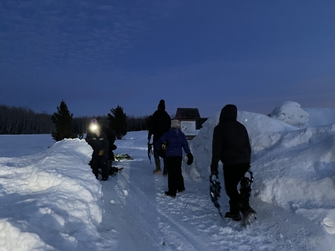 guests dressed in winter clothes carry snow shoes at dusk