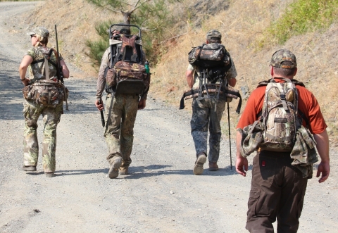 Four hunters with their packs in camo walking down a gravel road in sagebrush country.