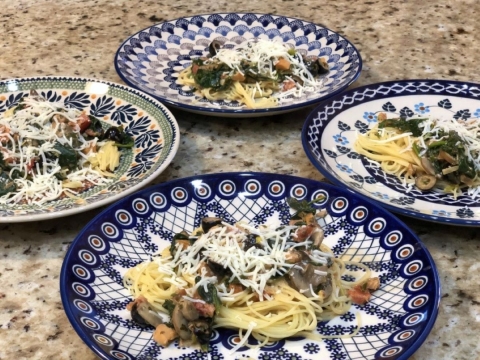 Four colorful plates with angel hair pasta topped with a creamy smoked trout sauce and Parmesan cheese.