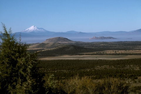 Landcape photo of a green basin with snowcapped mountain in the background.