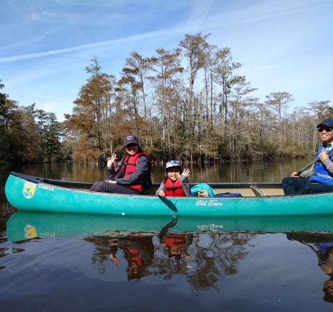 Family of two adults and a child smile from a canoe on the bayou