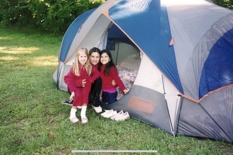 a young woman and two little girls smile while sitting next to a large camping tent