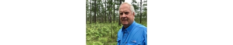 A close-up of Reese Thompson stands in a stand of young longleaf pines. 