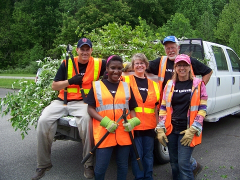 Five adults with orange vests and pruning shears standing by truck bed full of cut autumn olive