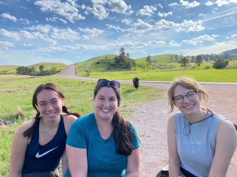 Three women pose for picture with a bison in the background