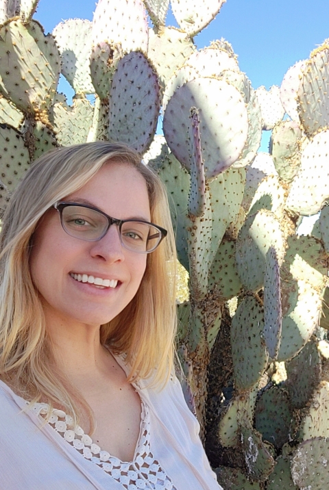 A woman stands in front of a cactus