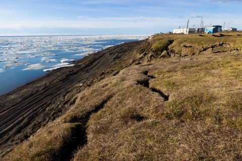 a few building sit on top of a grassy ridge overlooking the arctic ocean