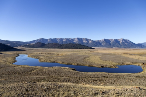An elevated view of a distant mountain range and a pond nearer in an arid landscape.