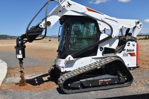 Maintenance Worker operating a Skid Steer with auger attachment to dig a hole.
