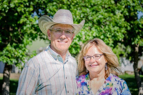 A man wearing a cowboy hat and a woman smile for the camera in front of green trees