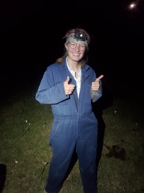 A bat biologists poses for picture during a night survey while wearing a headlamp and cave suit