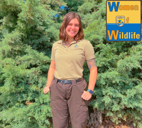 Kayla Feist stands in front of pine trees wearing a USFWS uniform. The WoW: Women of Wildlife logo is in the upper right hand corner of the photo. 