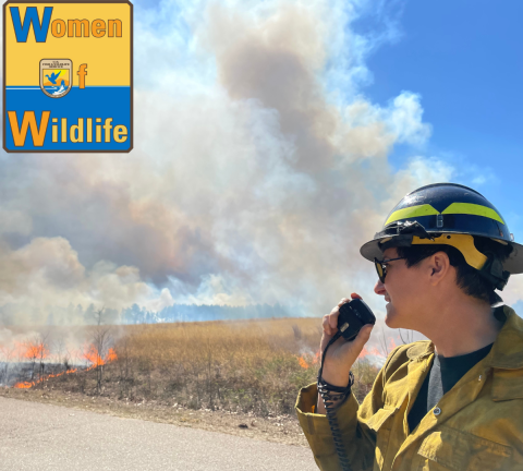 a person talking on a handheld radio while standing next to a dry grassy field that is burning and has smoke billowing into the air