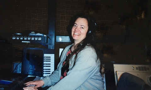 A woman with long dark hair, wearing a gray sweater, is seated at a keyboard