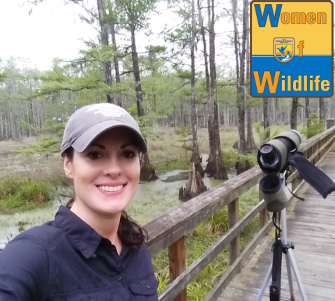 A woman standing next to a telescope on a boardwalk next to a swamp