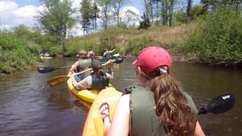 Women wearing life jackets and ball caps floating down the Blackwater River in canoes