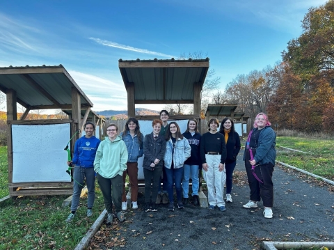 Ten students from Mt. Holyoke stand in front of targets at the Fort River Archery Range.