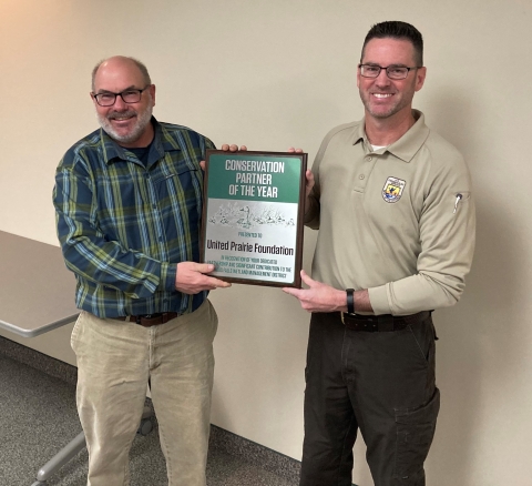 Two adults stand side by side holding an award plaque between them