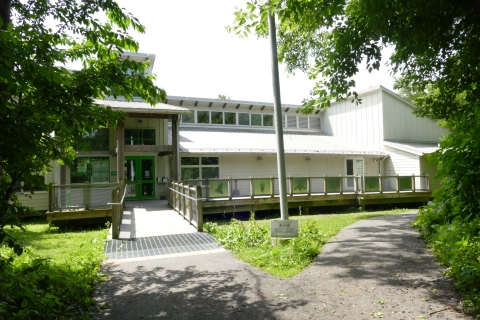 A white, angular, single-story building with green lawn and trees in the foreground