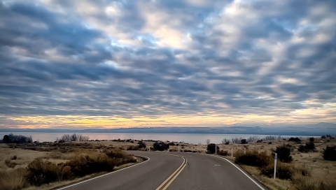 A road in the foreground with a lake and colorful sky with scattered clouds in the background