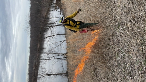 Wildland firefighter draws a line of fire away from a natural fire break - a lake - using a handheld drip torch. 