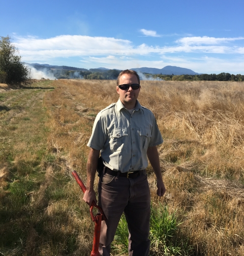 Man standing in a field with smoke from prescribed fire in the background