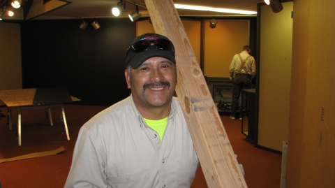A man smiling while carrying a wood column over his shoulder
