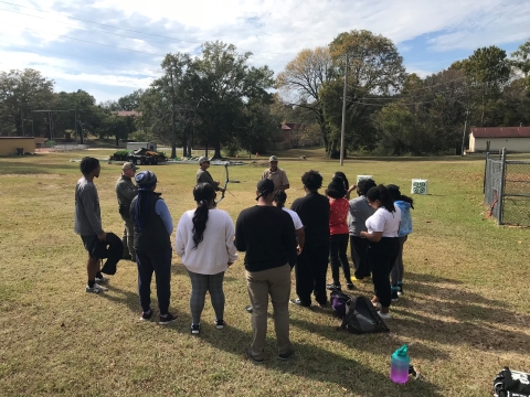 Bill Freeman and Tuskegee students stand in an open field with archery targets. 