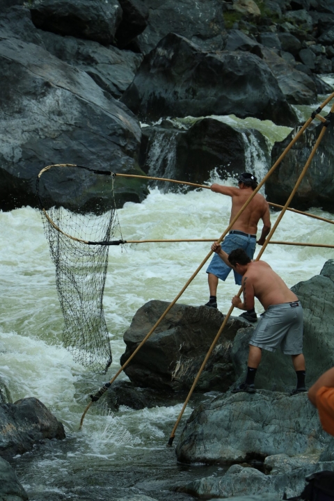 two tribal fisherman dip net fishing in river