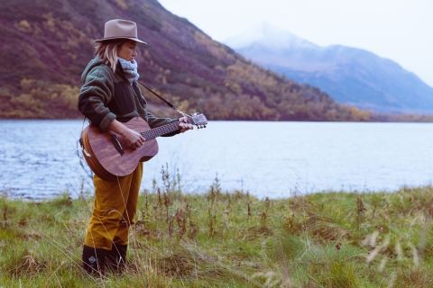 A woman playing guitar next to a lake