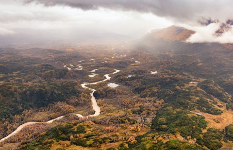 Aerial of a river winding through fall cottonwood trees in a valley surrounded by mountains